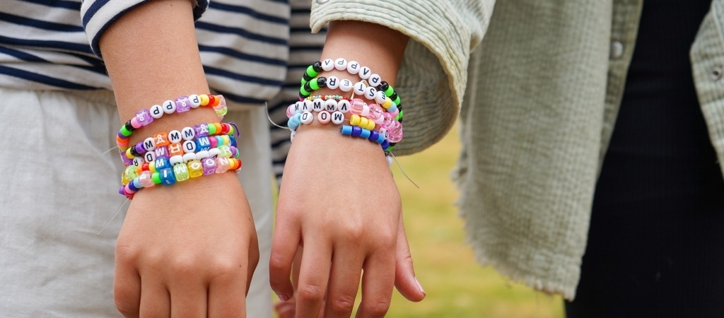 Två barn håller fram en hand som har armband runt handen. Armbanden är gjorda av pärlor i blandade 