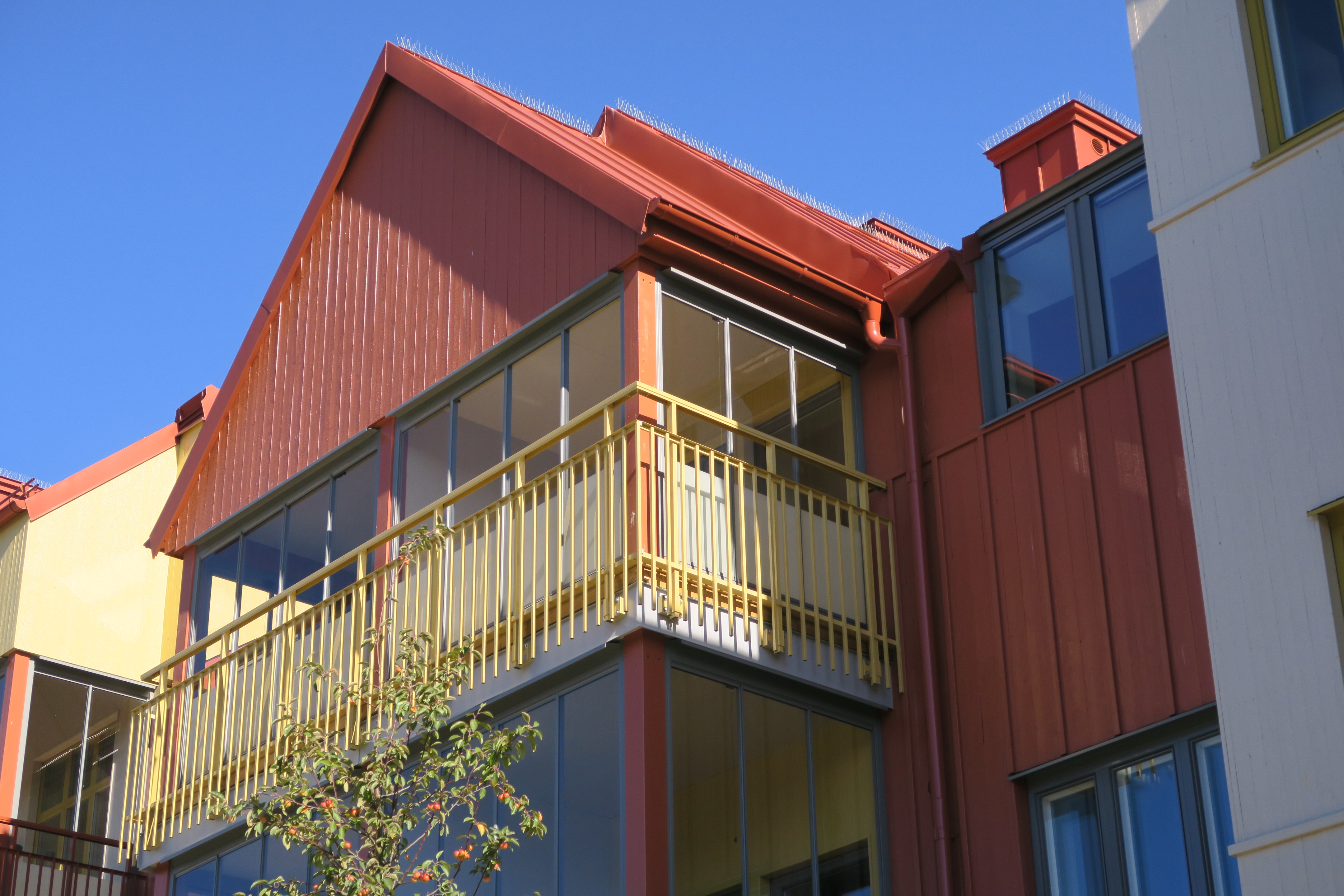 Bild på en balkong med gult smidesstaket och rött trätak.