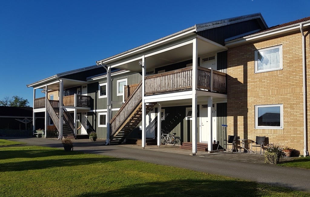 Tvåvåningshus i gult tegel med gröna trädetaljer och loftgång.