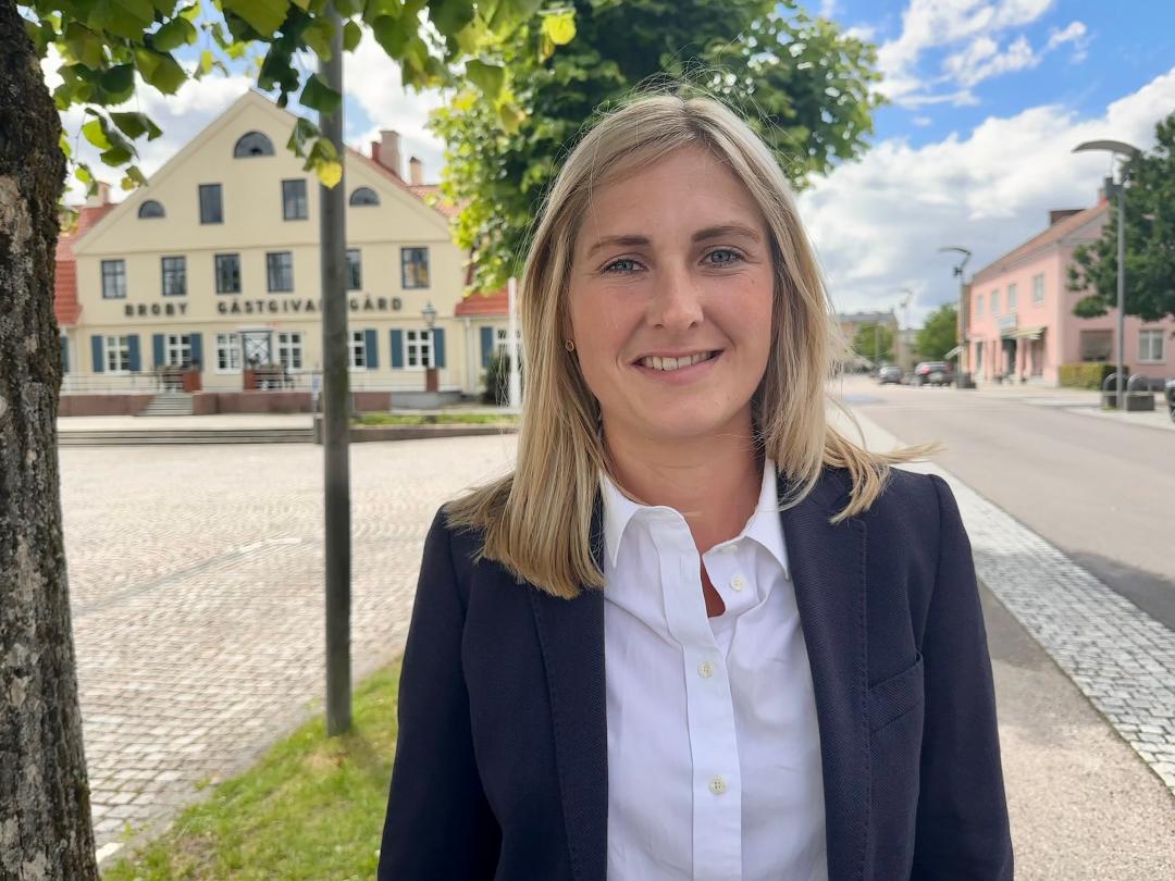 Bild på Kristina Nilsson. Hon står på torget i Broby med Broby Gästis i bakgrunden